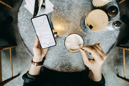 a women looking at data on her phone and drinking her coffee